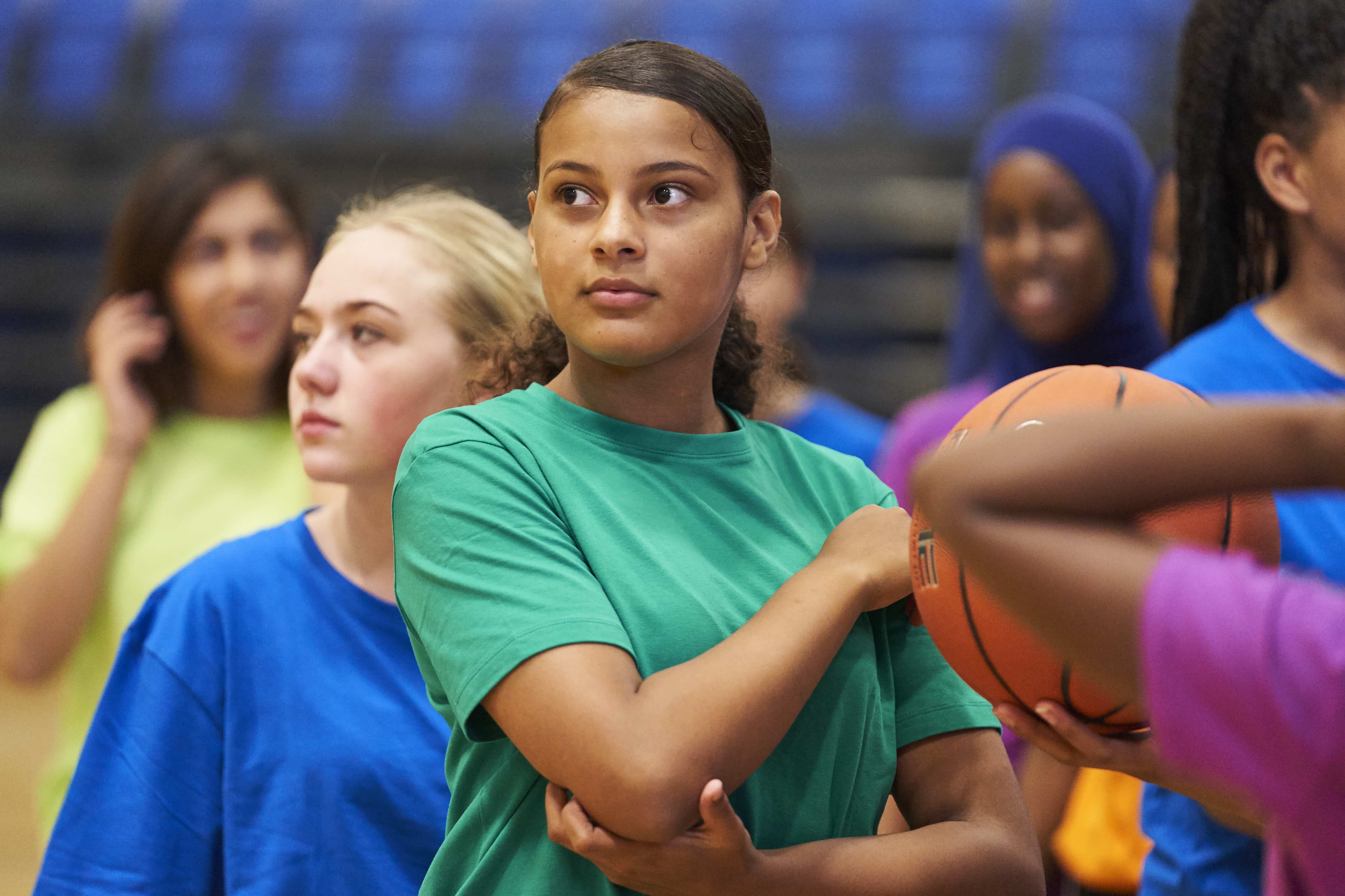 girls playing basketball indoors in different coloured t-shirts
