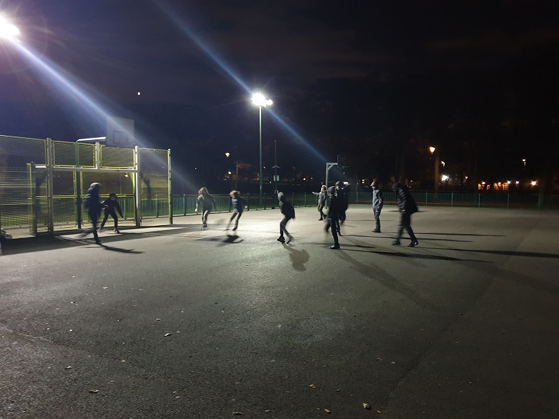 Young people playing football under floodlights