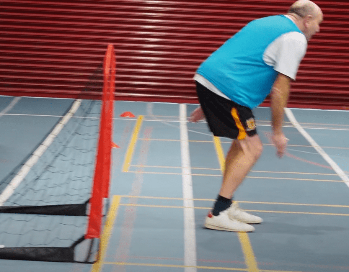 man in goal wearing a blue bib during walking football session in sportshall. 