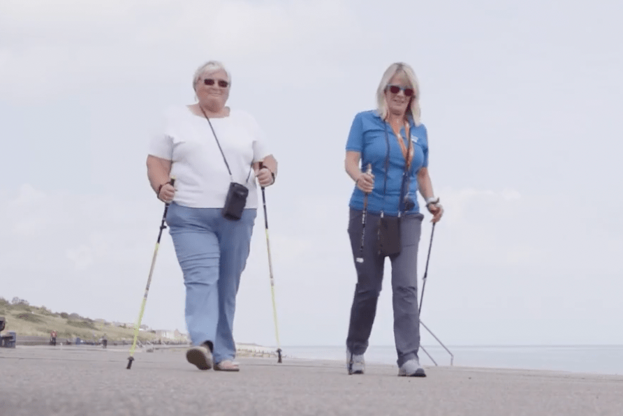 Margaret walking with the Nordic poles and trainer Julie along the seafront