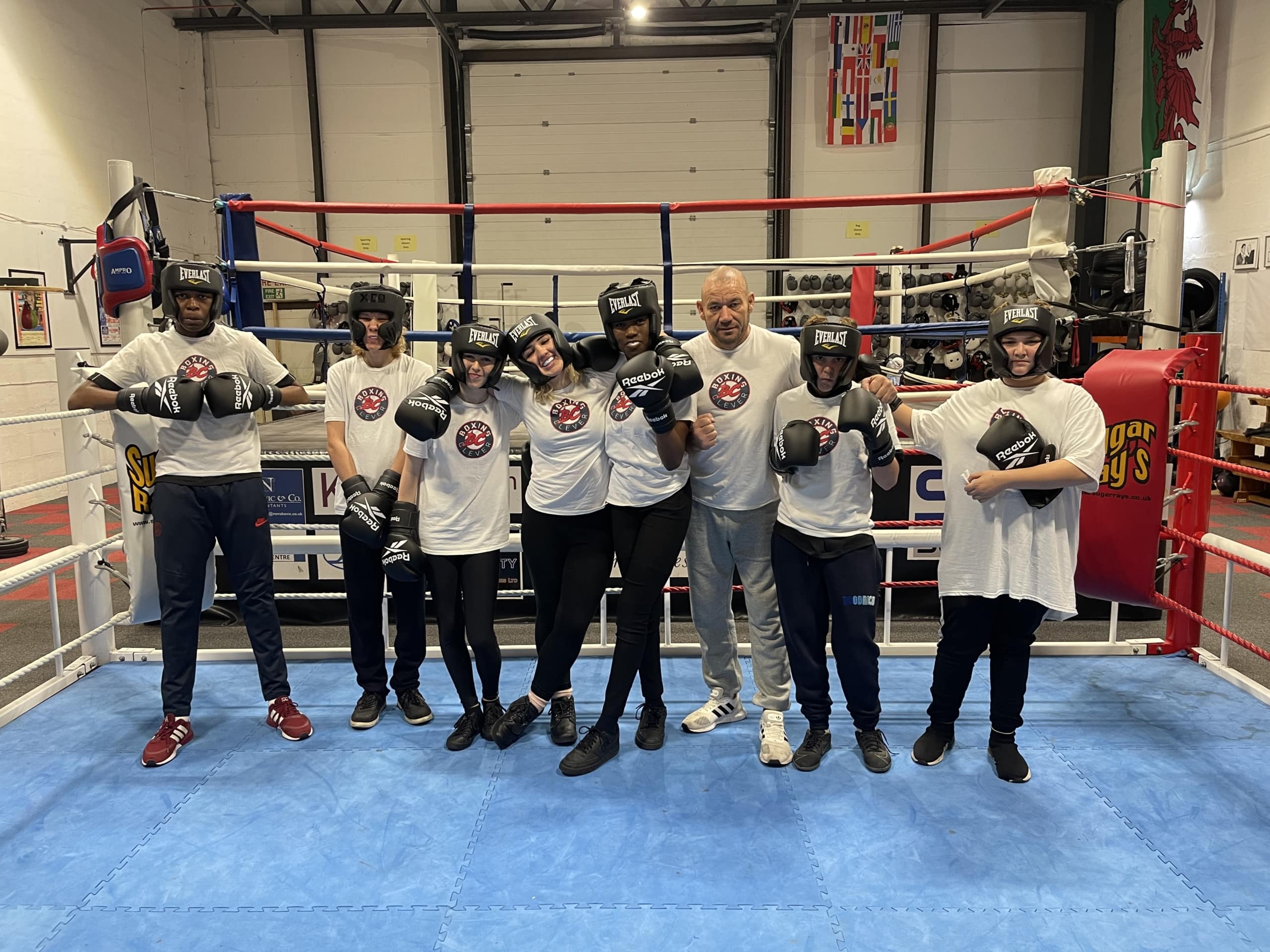 group of young people in tshirts and boxing head guard and gloves standing in a blue boxing ring