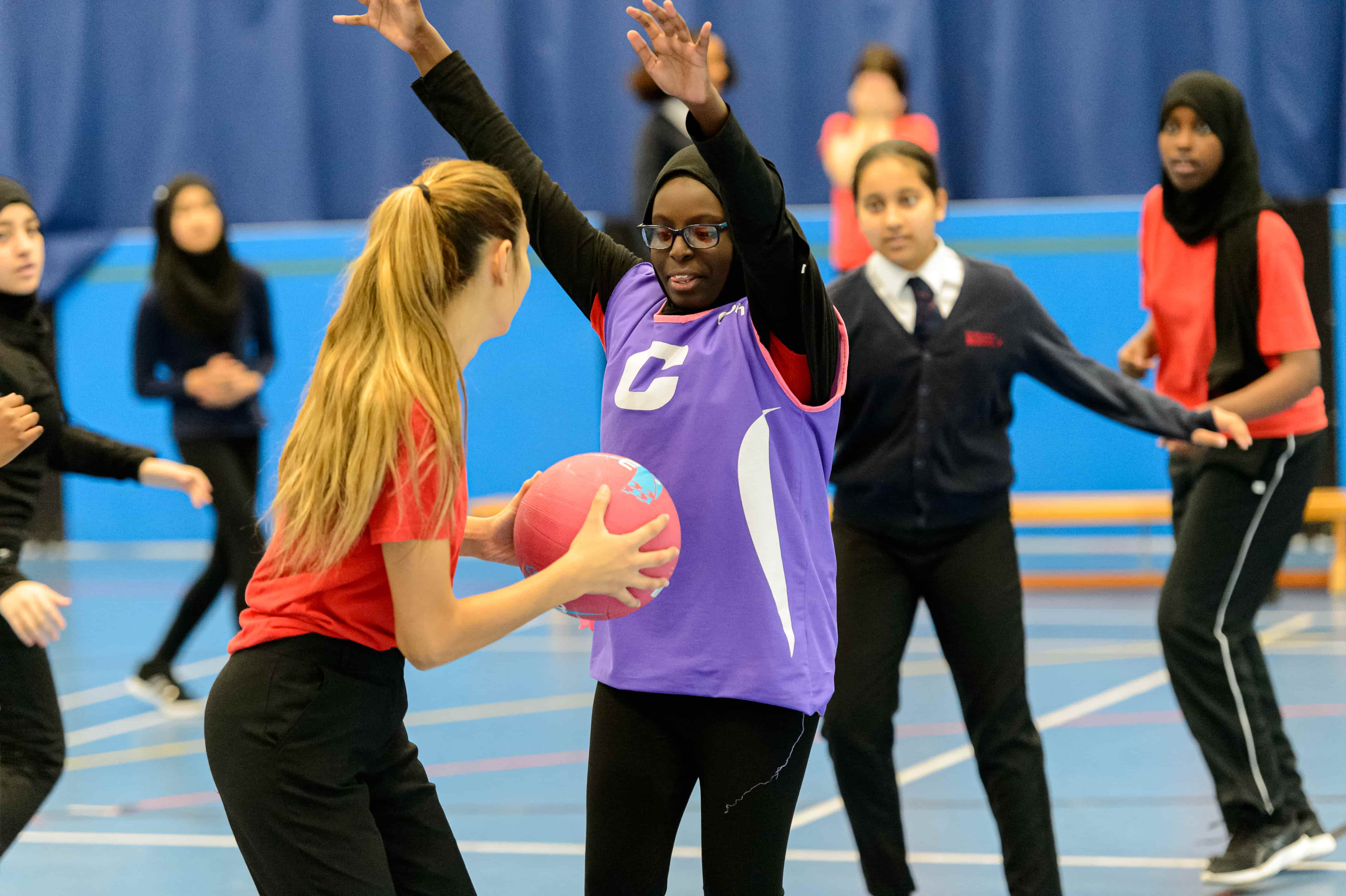 girls in a sports hall enjoying playing netball. 
