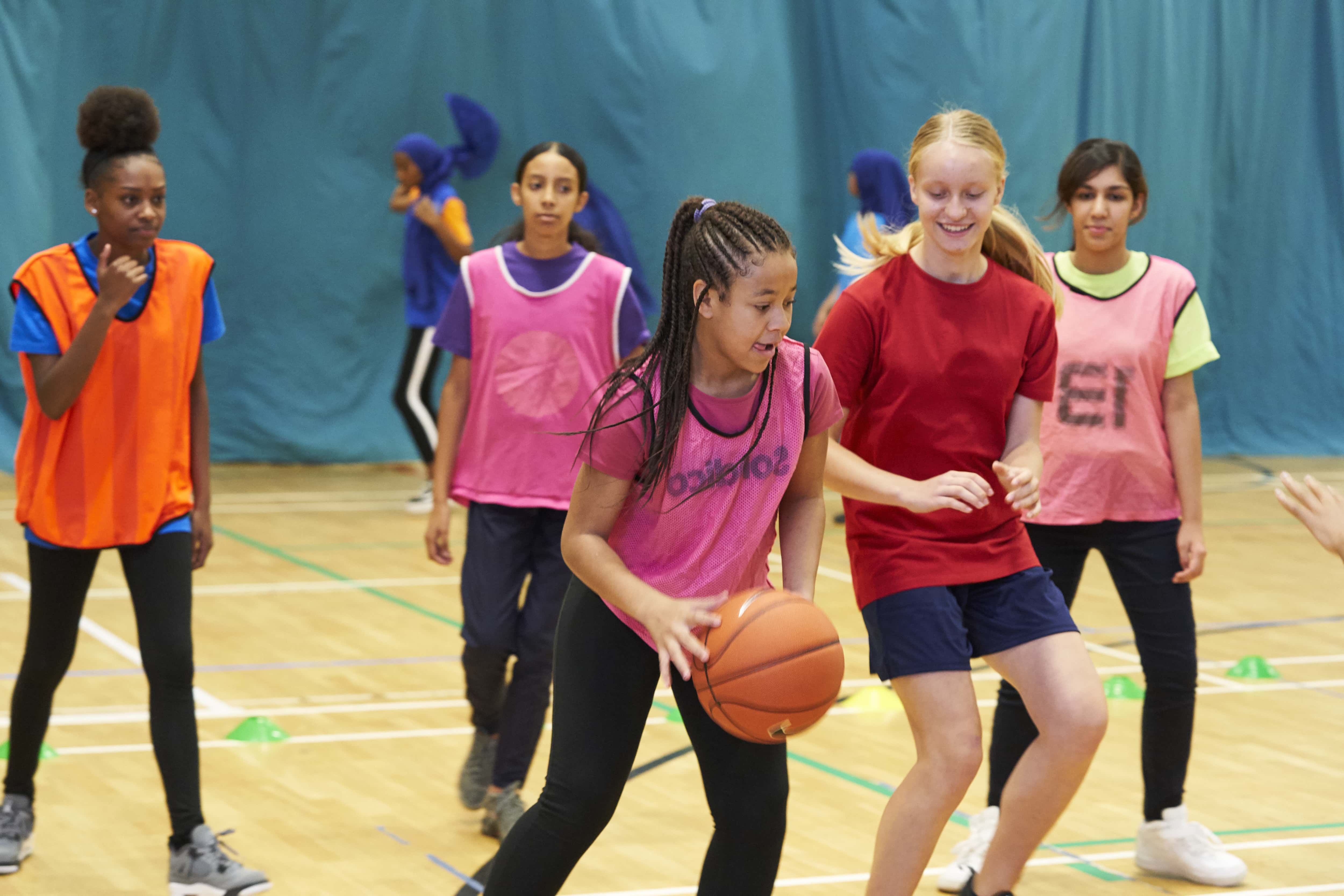 teenage girls playing basketball in a school hall