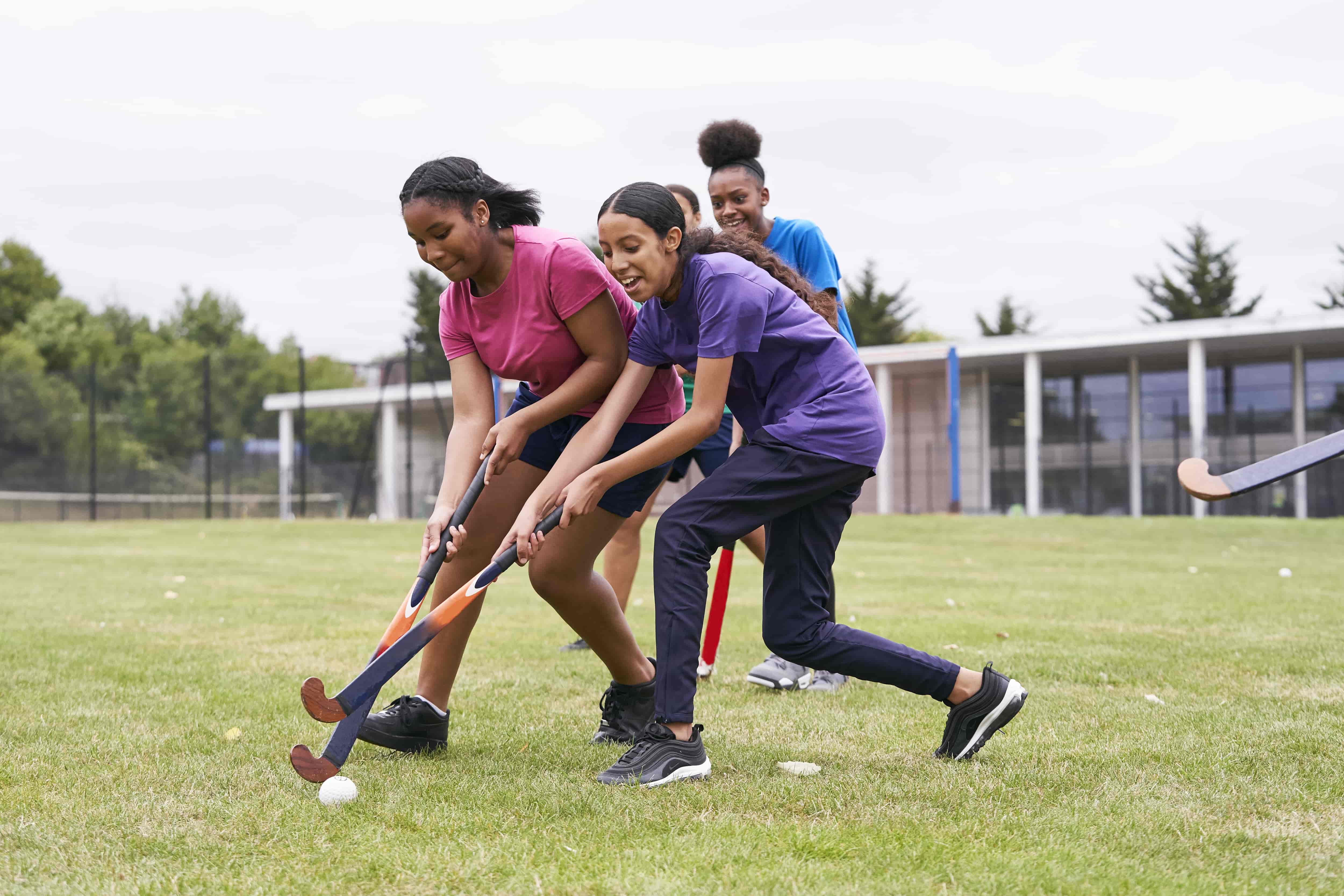 Four teenage girls playing hockey on outdoor school pitch 