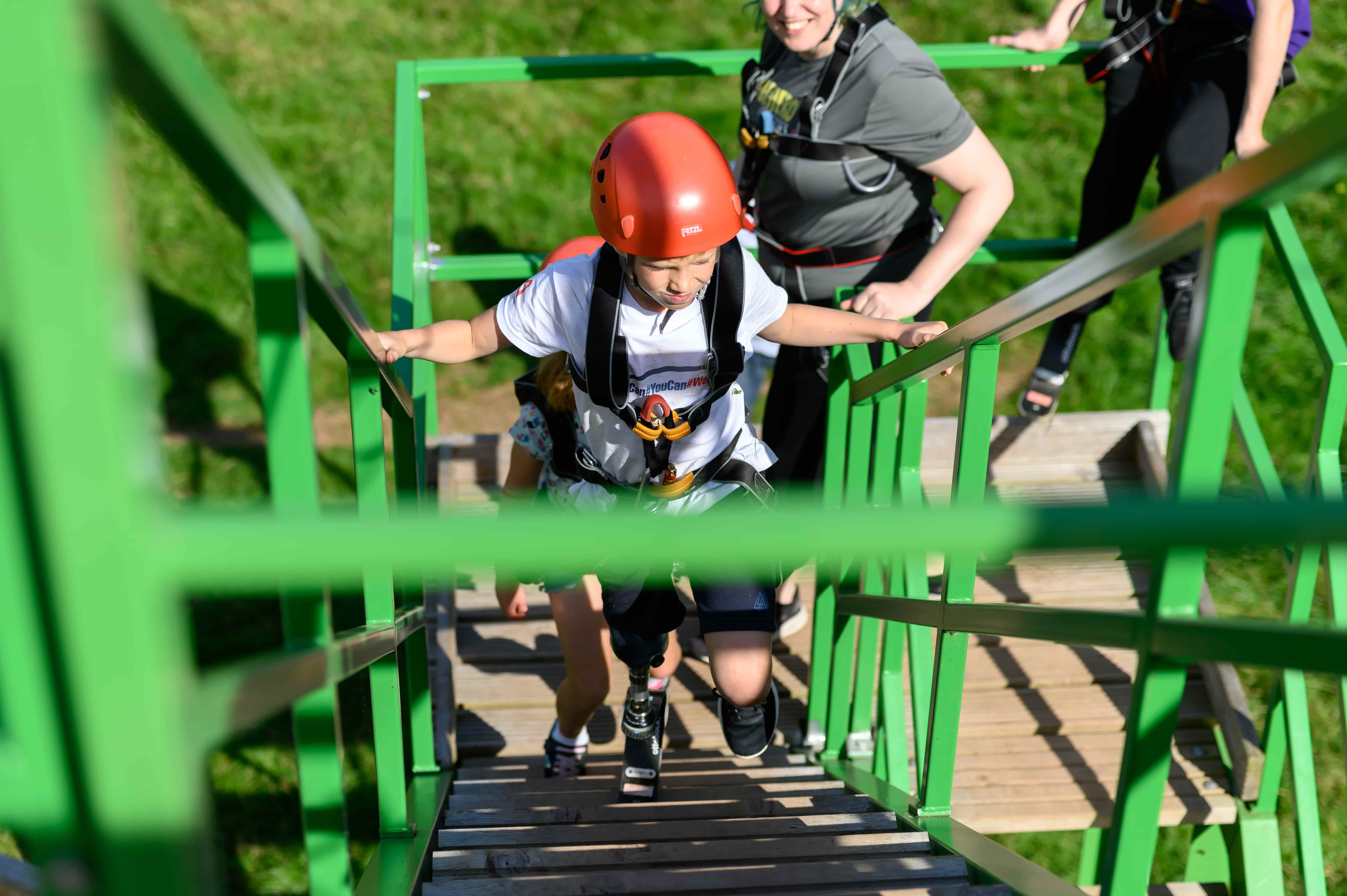 disabled young boy walking up a ladder on an obstacle course