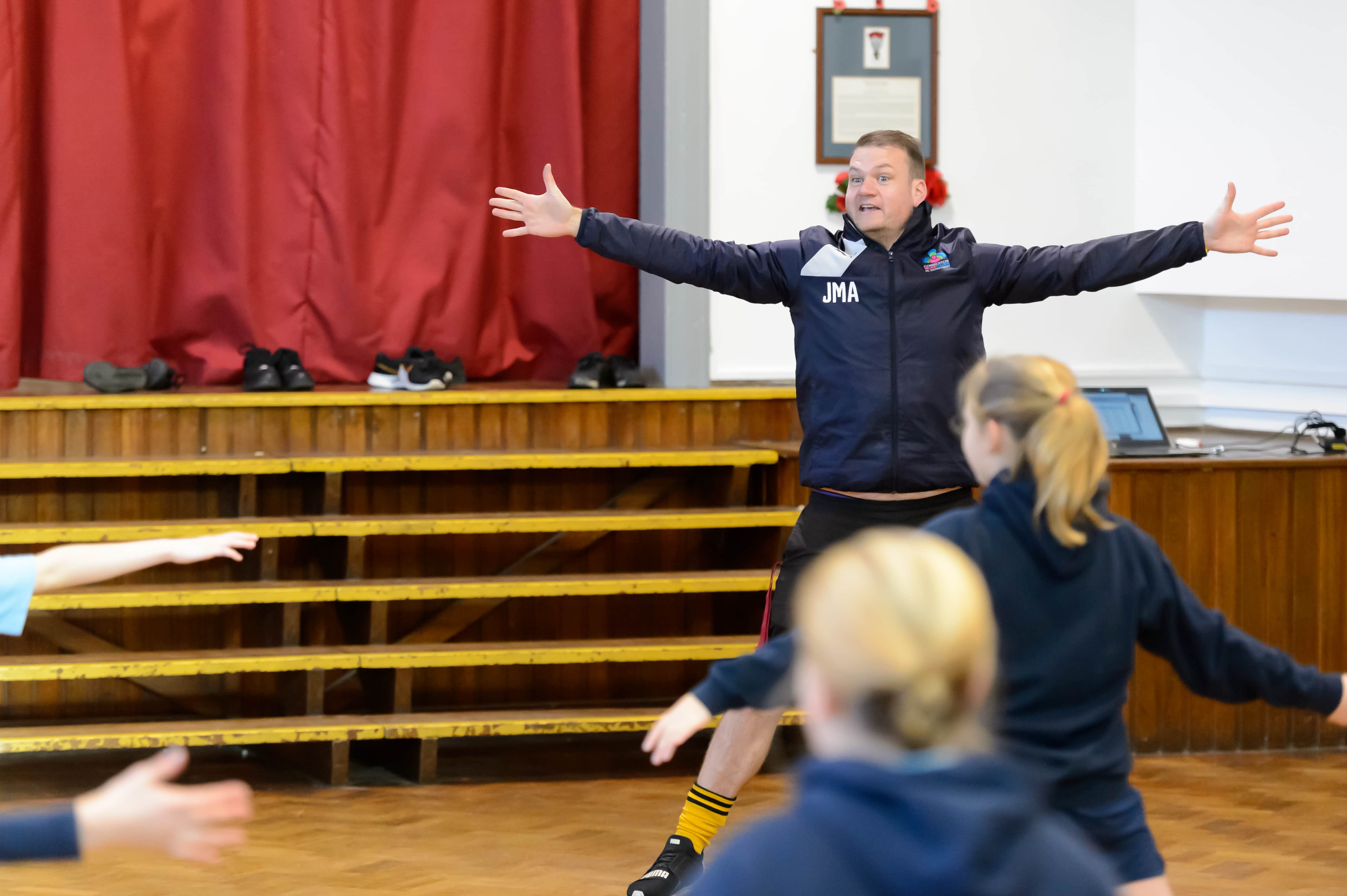 male teacher doing star jumps with with a class on young people