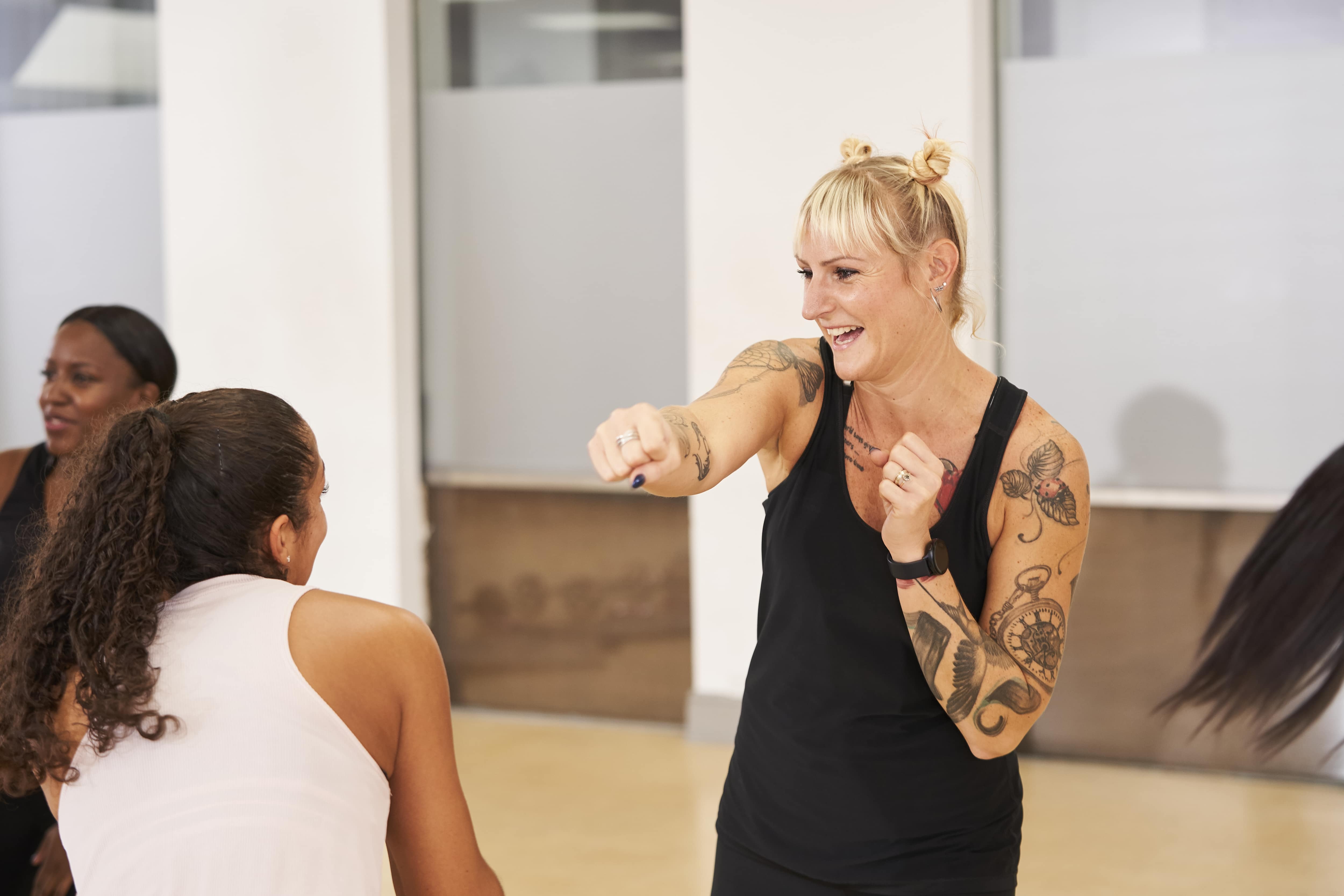 female instructor in a black vest top with tattoos on her arm leading an exercise class