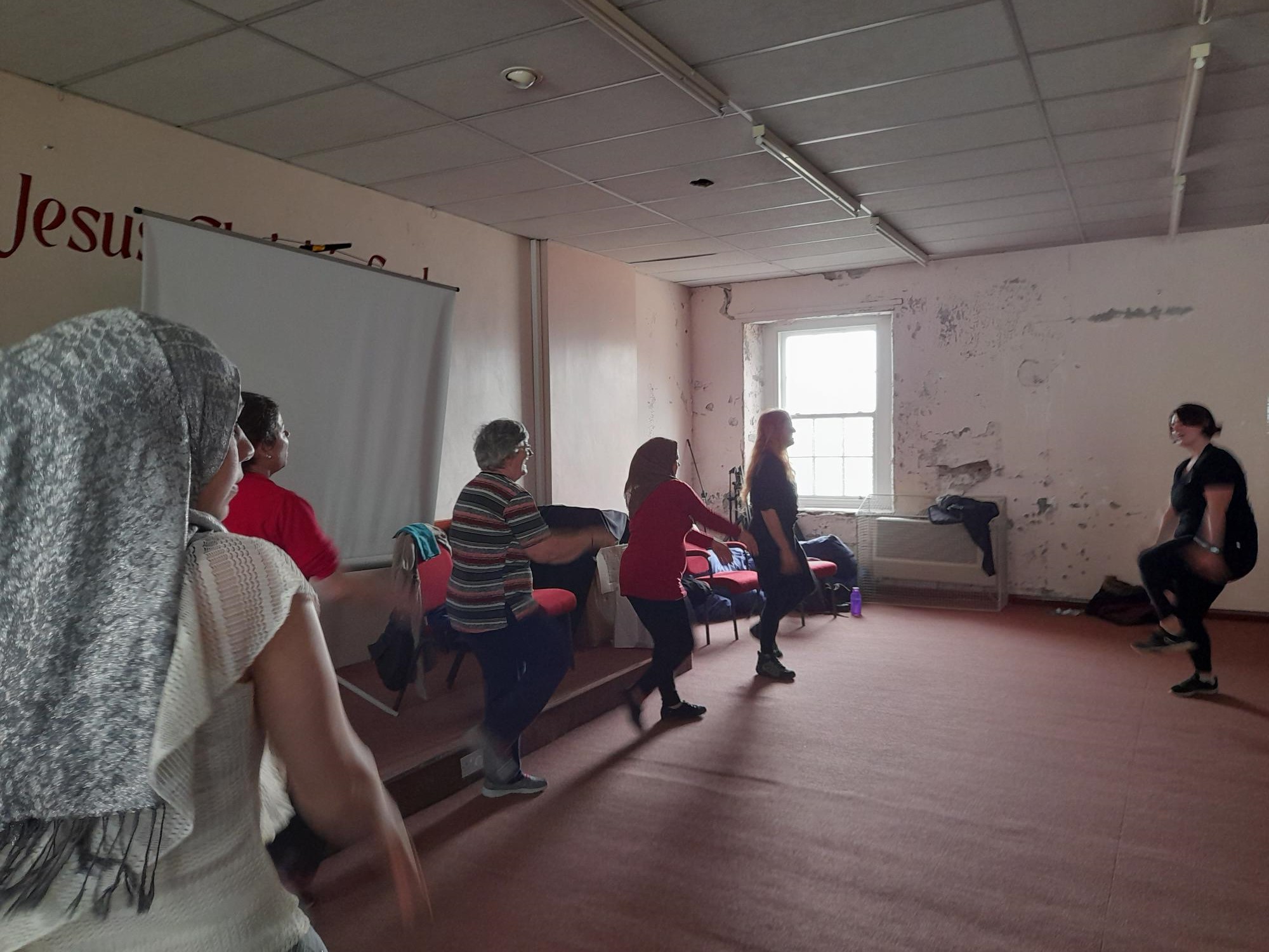 group of female refugees taking part in movement class in community hall