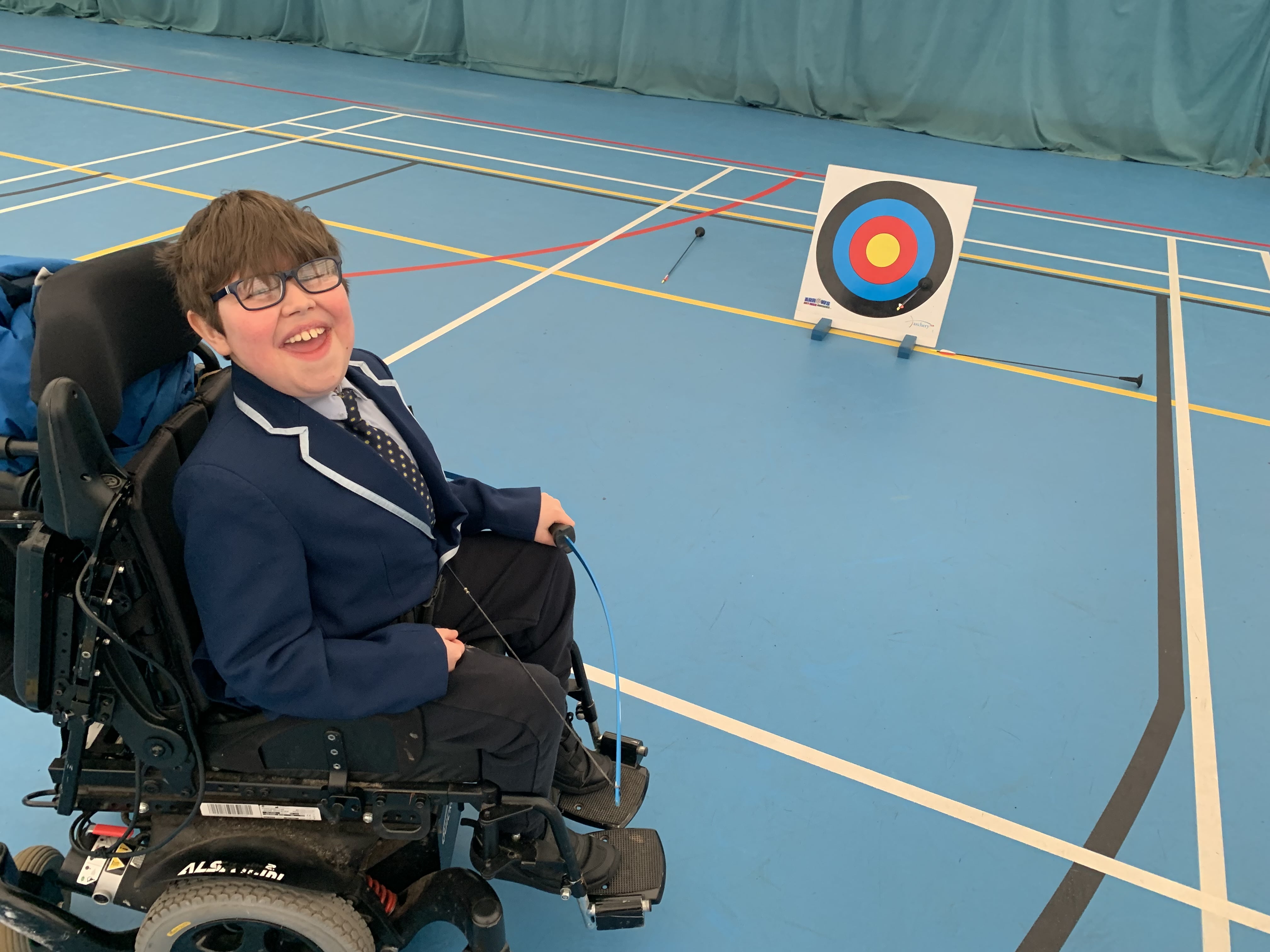 Young boy in a wheelchair in sports hall playing archery