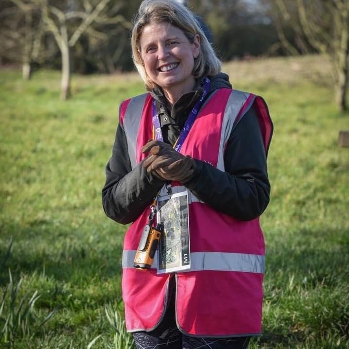 female in pink high visibility vest smiling in a outdoor grass space