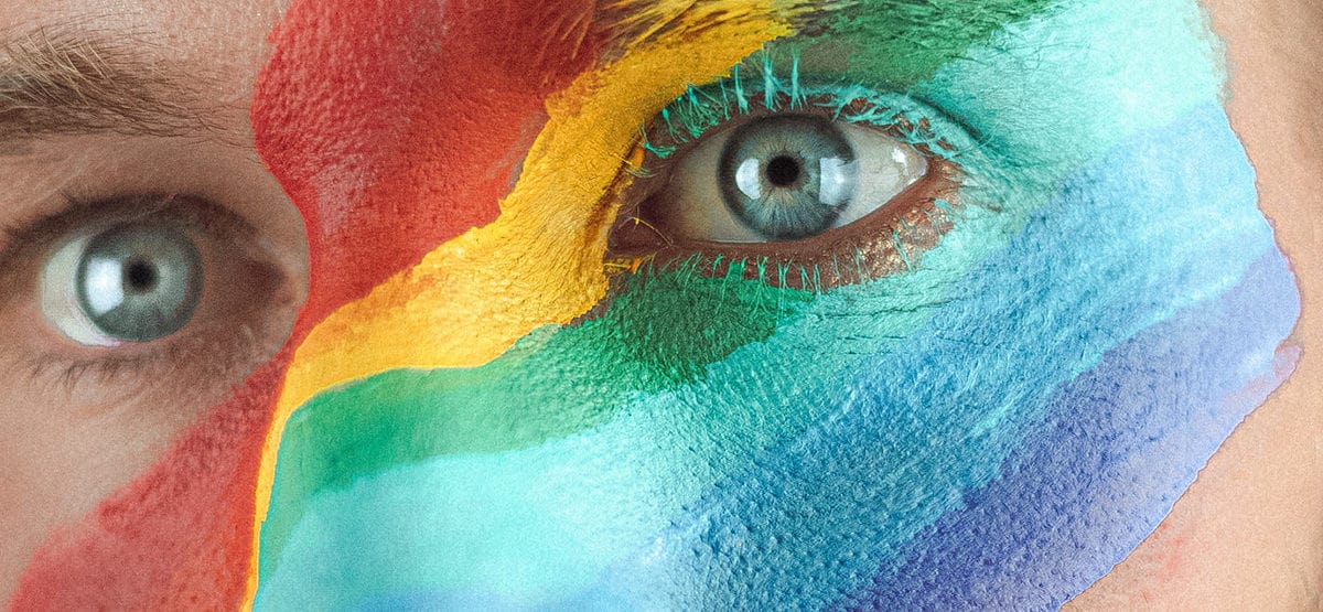 close up of a persons face with a rainbow colours painted over the bridge of the nose and right left eye