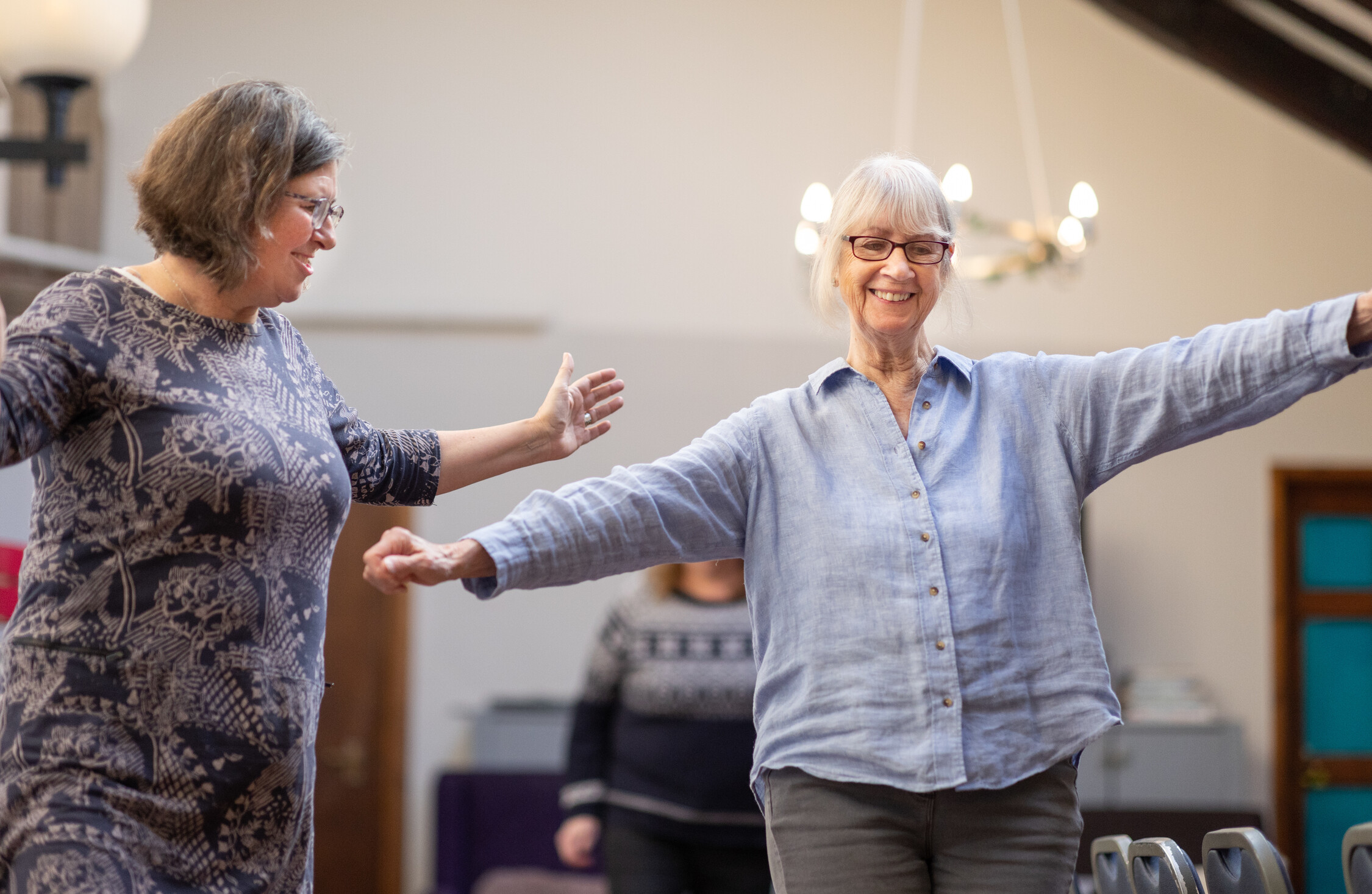 two older females taking part in a exercise class in a community hall 