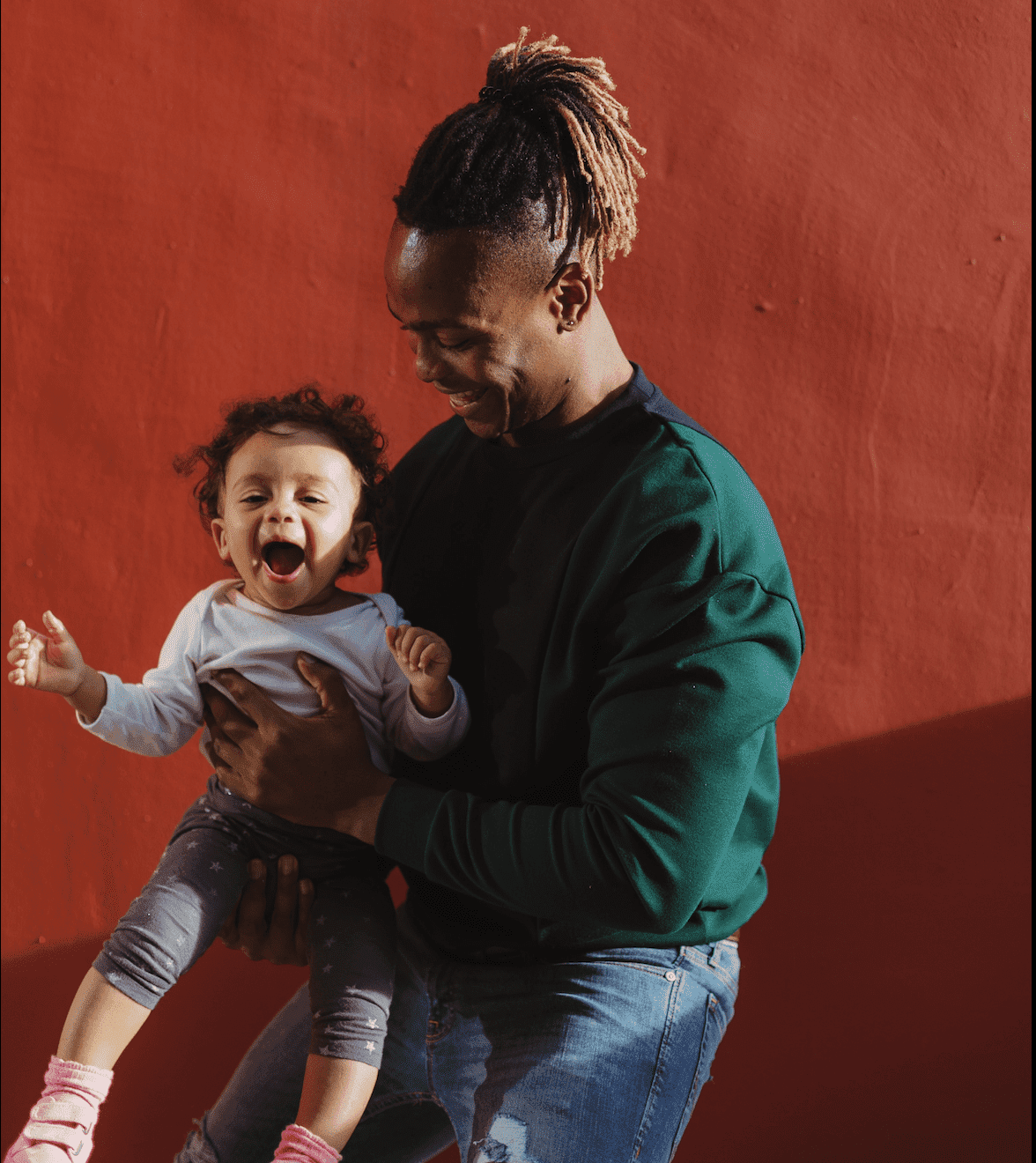 black man with dreadlocks holding his small daughter who is laughing in his arms 