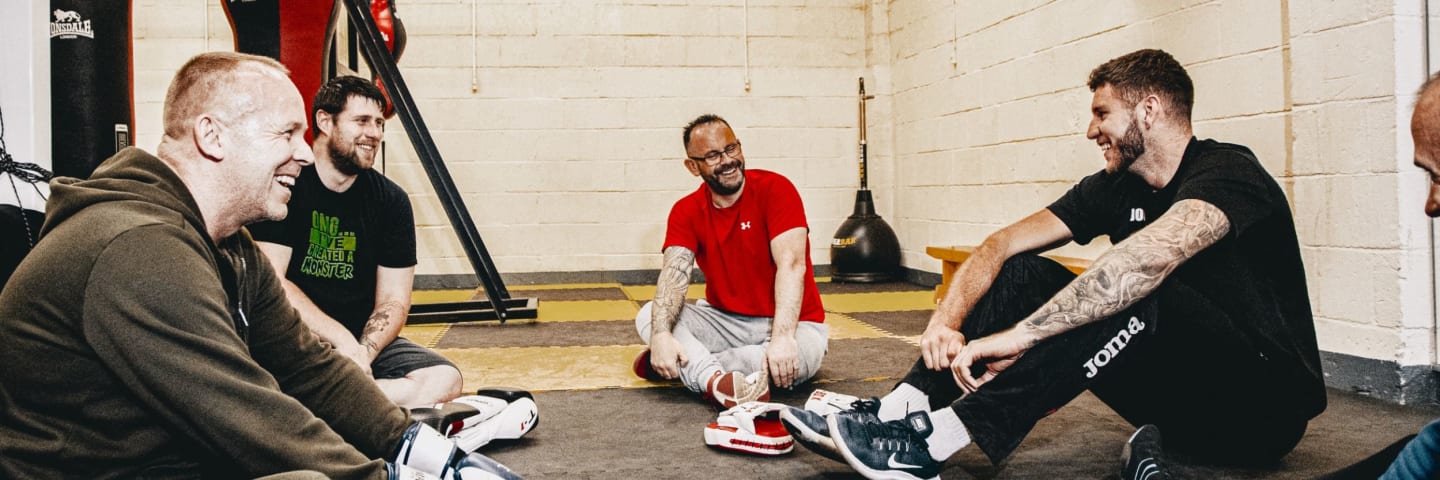 group of 4 men sitting on the floor in boxing gym having a friendly chat