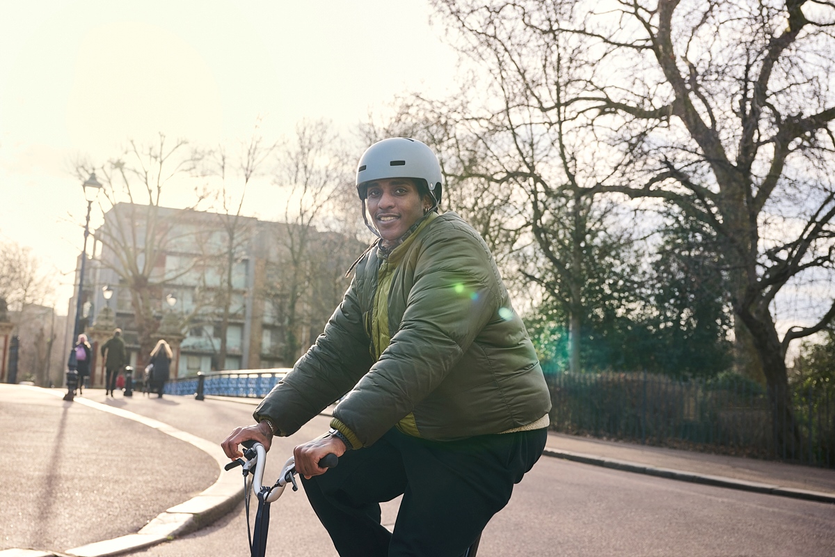 A man in a green jacket is sat on a bike. He is wearing a helmet.