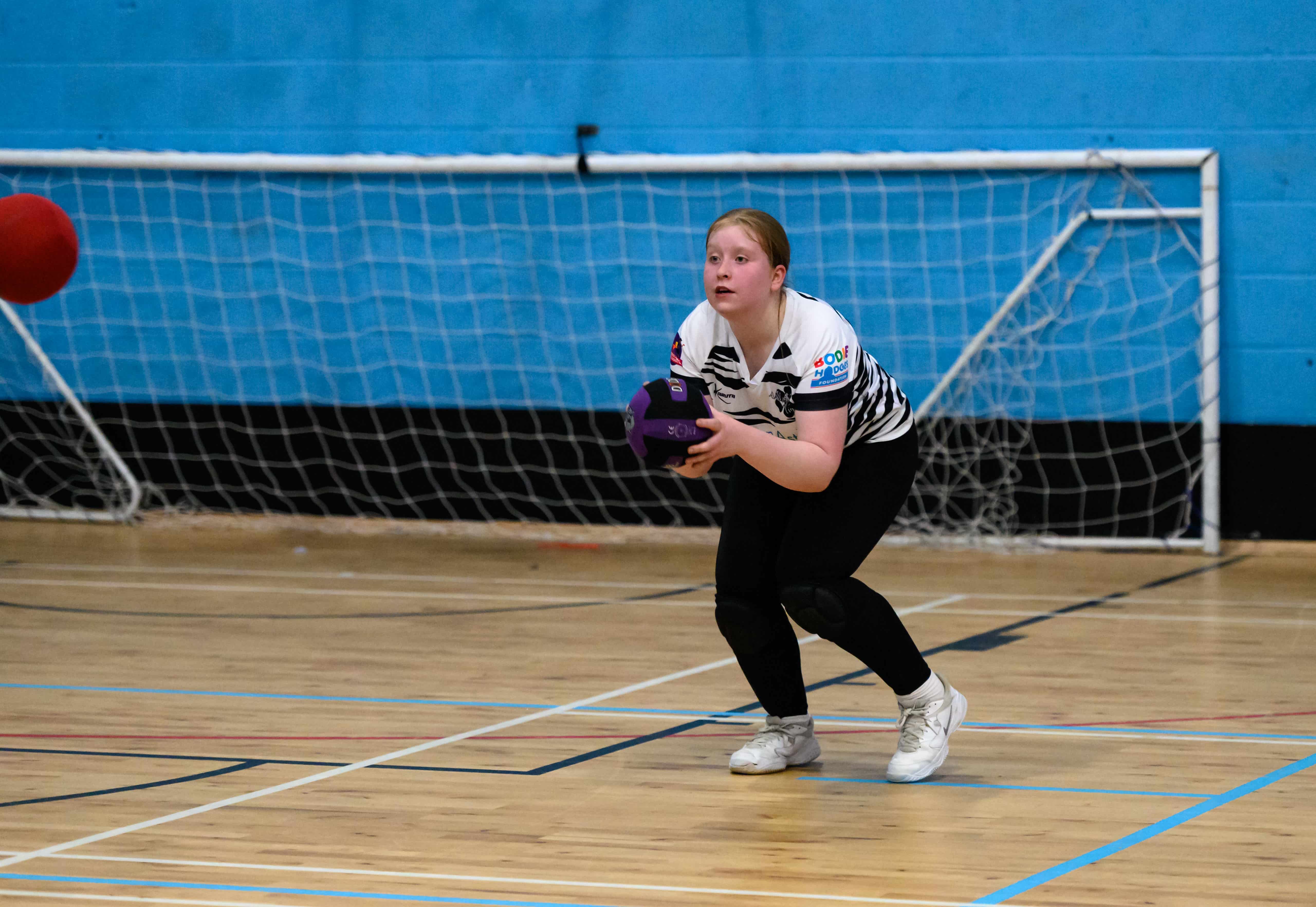 Girl in black leggings and white t-shirt holding a ball in sportshall