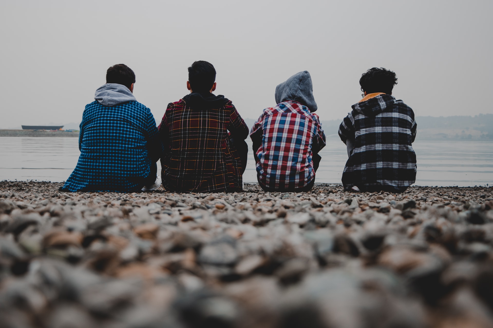 4 males sitting on the beach with their backs to the camera facing the sea