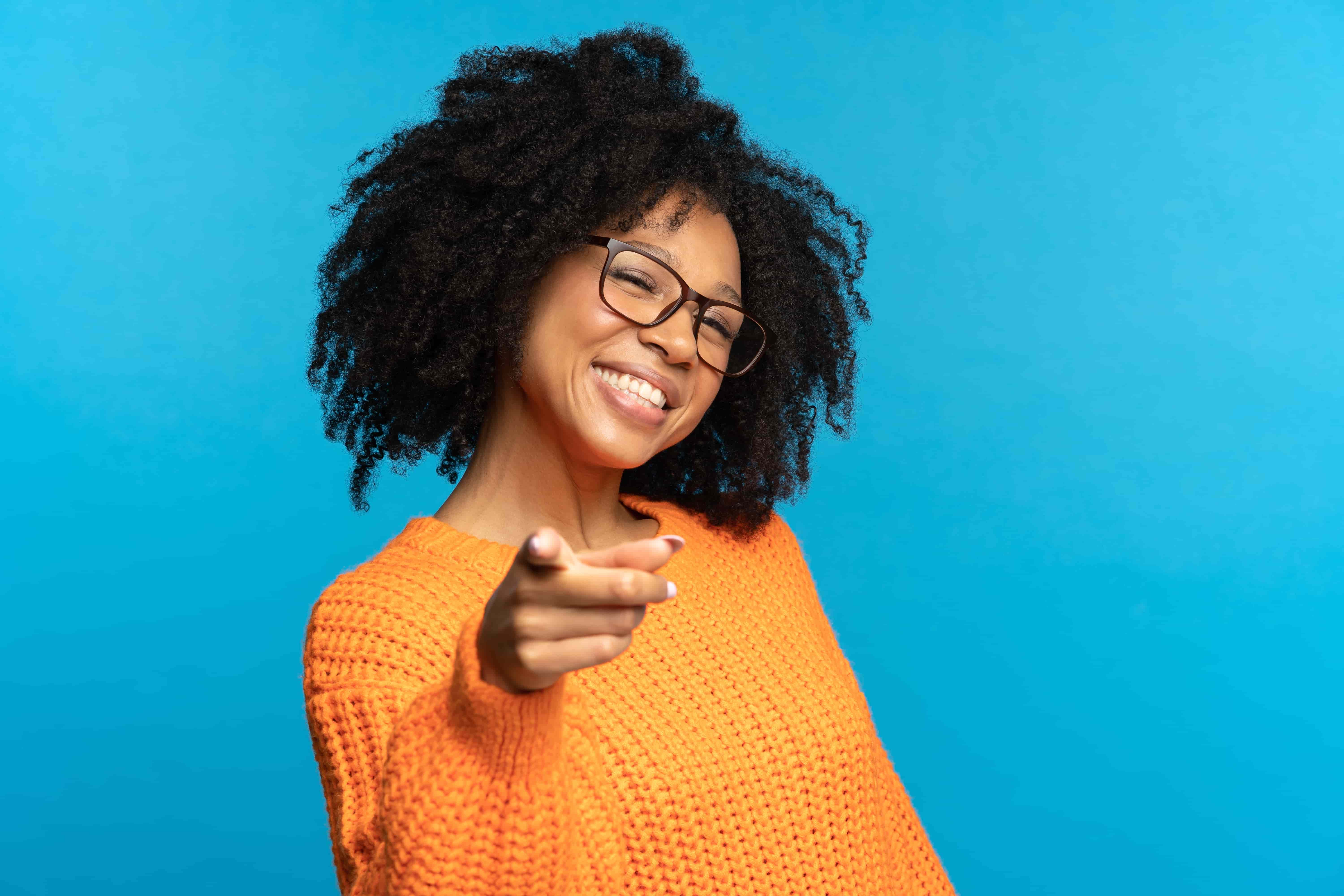 Black female smiling in a orange jumper pointing at the camera