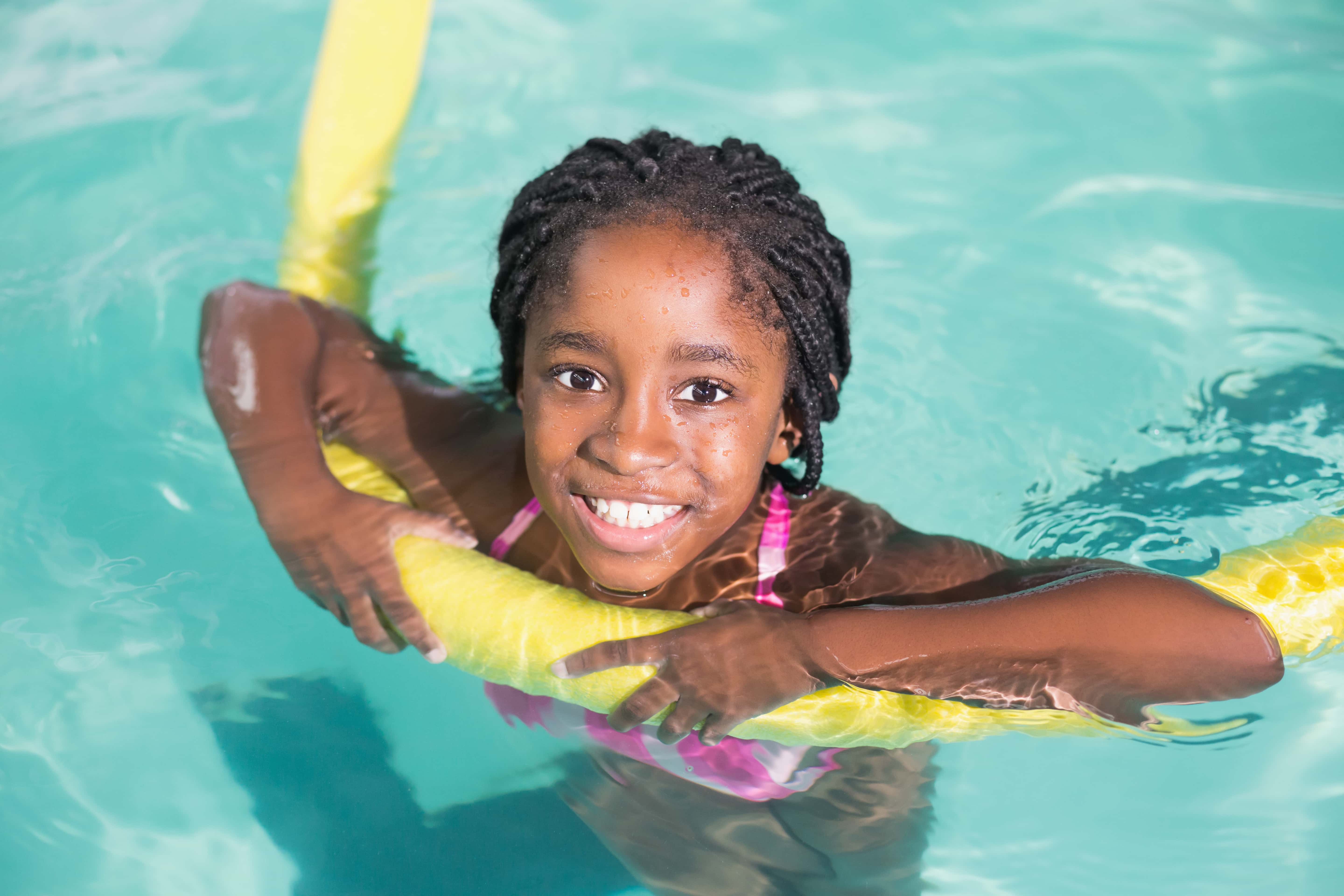 black girl smiling in a swimming pool holding a yellow long float 