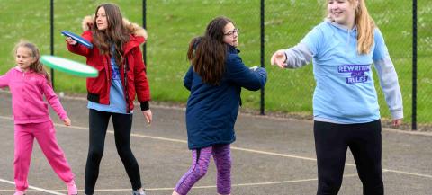 group of primary aged girls in a playground learning to throw a frisbee 