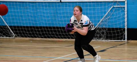 Girl in black leggings and white t-shirt holding a ball in sportshall