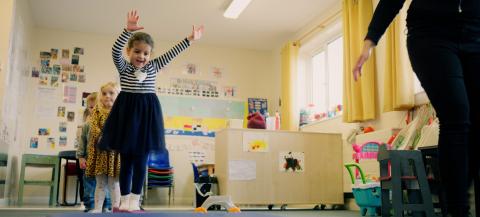 a young girl in a striped skirt smiling as she walks across a low balance bean in a nursery room