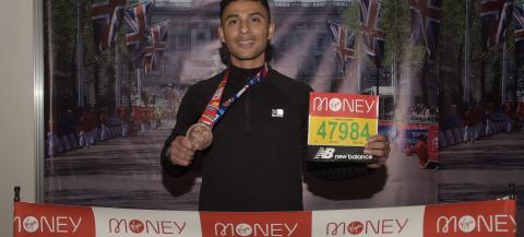 Bahr showing his London marathon finishers medal and number in front of a picture of London