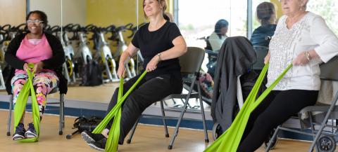 three women involved in a seated exercise class using bands 