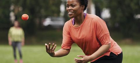 black female in active wear throwing a small orange ball in the park