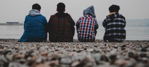 4 males sitting on the beach with their backs to the camera facing the sea