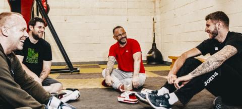 group of 4 men sitting on the floor in boxing gym having a friendly chat