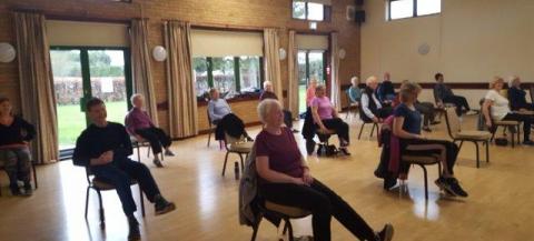 an older group of people doing chair based activity in hall