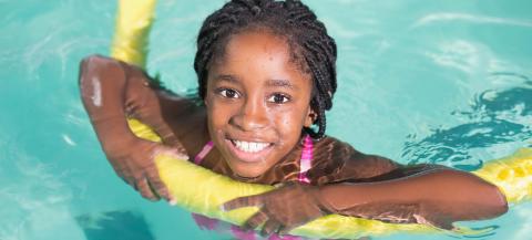 young black girl in a swimming pool lying on her front using a long yellow float