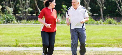 older male and female smiling whilst jogging in green space