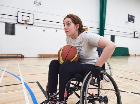 teenage girl in white t-shirt playing wheelchair basketball in indoor hall 