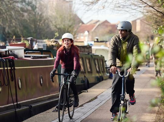 Two adults cycling down a canal path dressed in coats. 