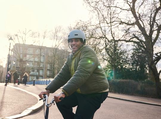 A man in a green jacket is sat on a bike. He is wearing a helmet.