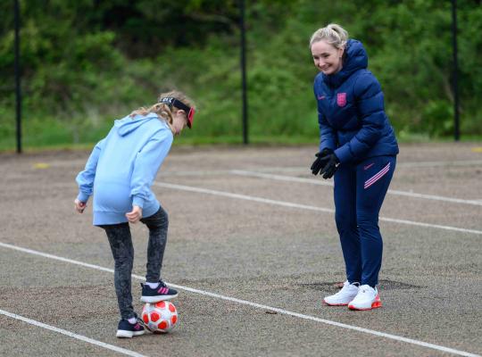 A female football coach encouraging a young player in a school playground