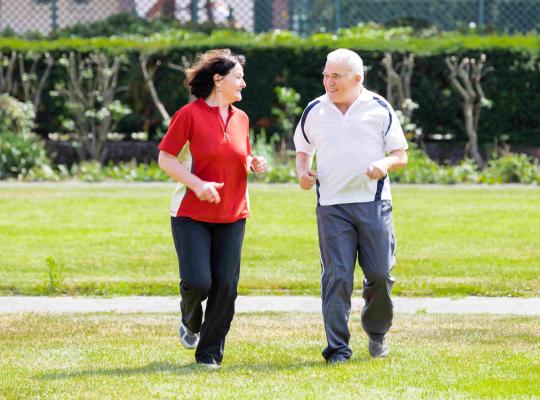 older male and female smiling whilst jogging in green space
